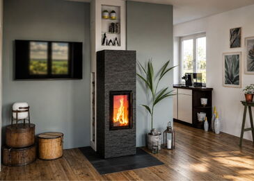 Gesamtansicht des geraden Monolith Kaminofens mit dunkler Natursteinverkleidung und integriertem Wandregal für Holz und Dekoration.