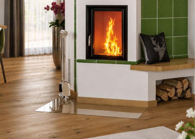Nahaufnahme des brennenden Feuers hinter der großen Sichtscheibe sowie der transparenten Glas-Bodenschutzplatte auf hellem Parkett.