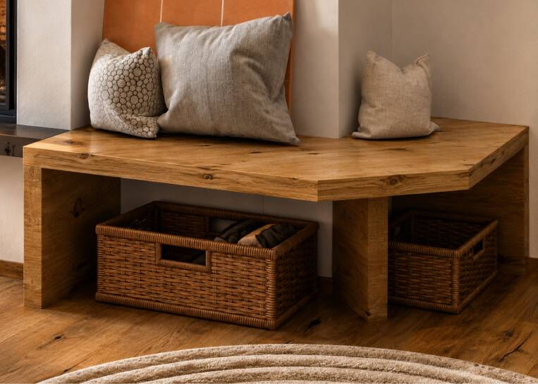 Nahaufnahme der massiven Holz-Sitzbank mit praktischen Weidenkörben zur Aufbewahrung im Kamin-Sockelbereich.
