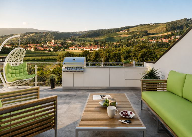 Panorama-Ansicht einer weißen Edelstahl-Außenküche mit Napoleon Pro 665 Grill vor einer weitläufigen Hügellandschaft.