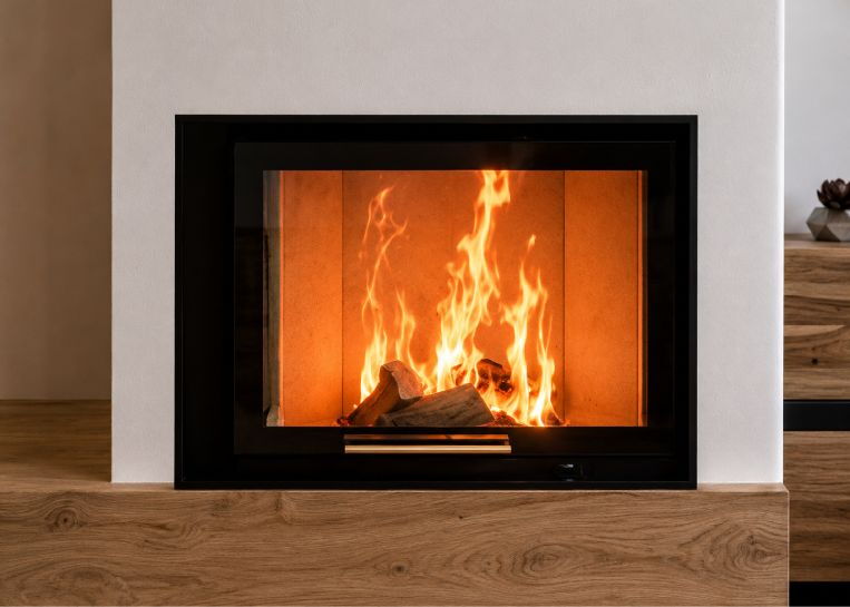 Nahaufnahme des brennenden Holzfeuers hinter dem Eckglas, umrahmt von der glatten Oberfläche der Sinterkeramik.
