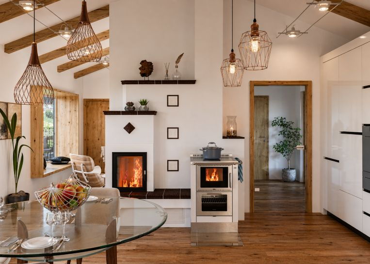 Gesamtansicht der Anlage mit weißer Feinkeramik und Metallteilen. Ein zentrales Holzlager verbindet den Kamin optisch mit dem Pertinger Herd.