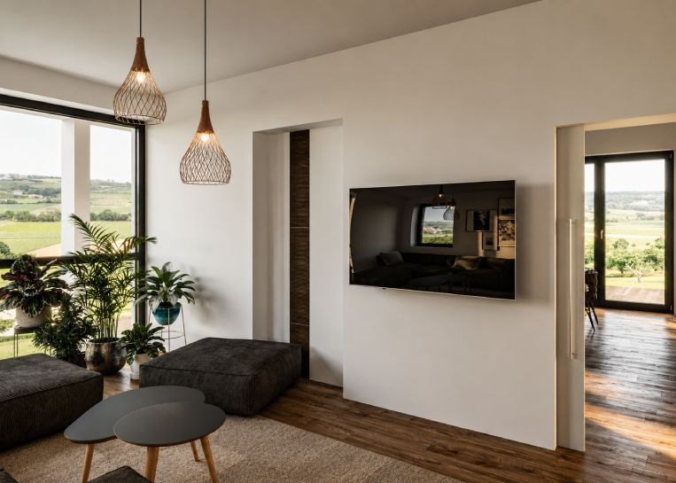 Blick in den Wohnbereich mit wandmontiertem TV und exklusiven Pendelleuchten, passend zum Ofendesign.