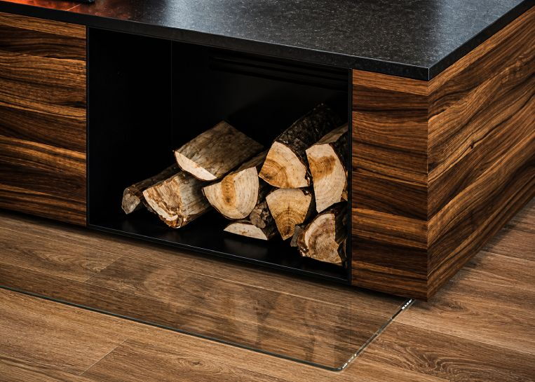 Nahaufnahme der schwarz lackierten Metall-Holzlagerbox, die bündig in den mit Naturholz verkleideten Sockel integriert ist.