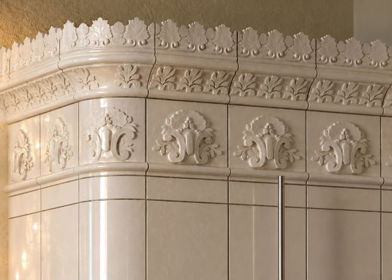 Nahaufnahme der kunstvoll verzierten Simskacheln mit floralen Relief-Ornamenten und glänzender heller Glasur.