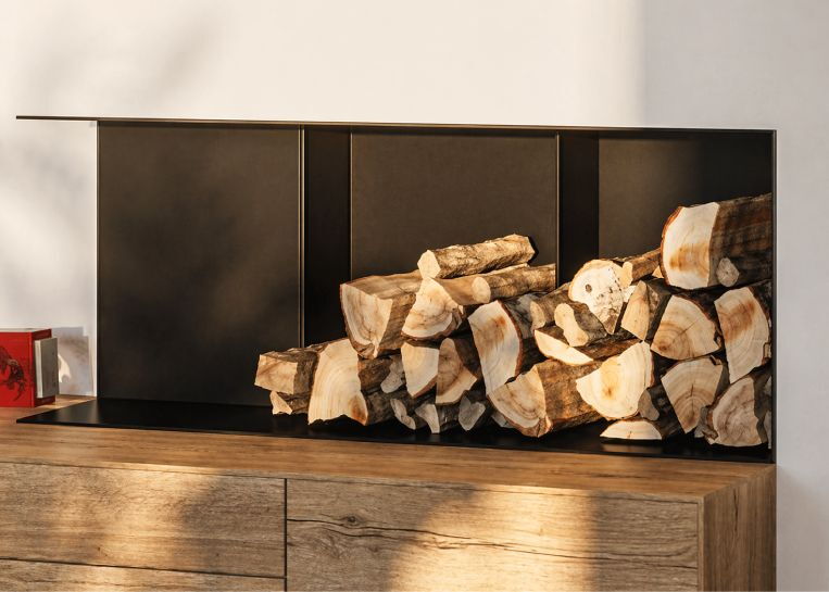 Nahaufnahme des großzügigen Holzlagers mit schwarzer Innenverkleidung, das bündig in den Kaminbau integriert ist.