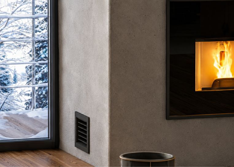 Detaillierte Ansicht des dezenten schwarzen Lüftungsgitters in der Kaminwand zur Verteilung der Warmluft in andere Räume.
