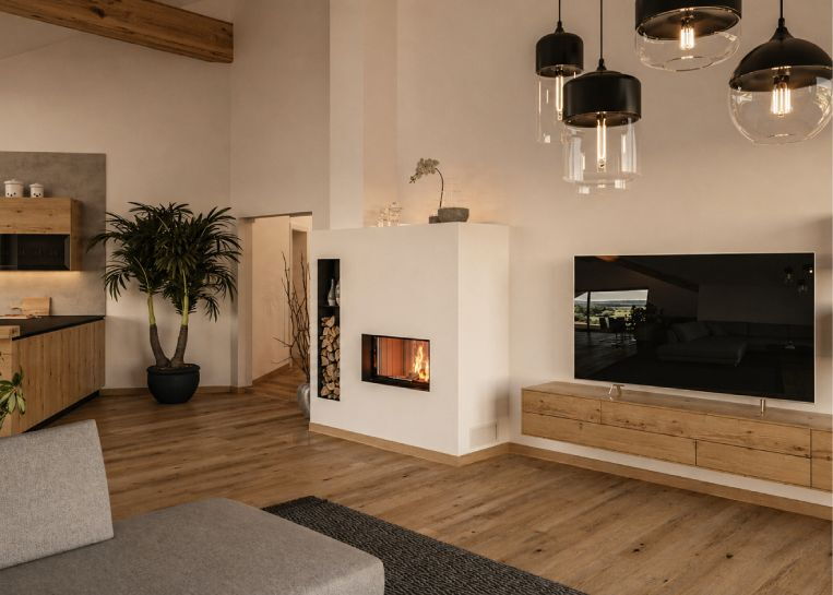 Perspektive auf den schlichten Kamin im Kontext eines modernen Wohnzimmers mit offener Küche, Holzfußboden und stilvoller Beleuchtung.