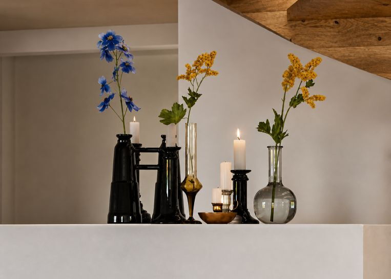 Detailansicht der mattweißen Keramikabdeckung mit stilvollen schwarzen Vasen, gelben Blumen und Kerzenständern.
