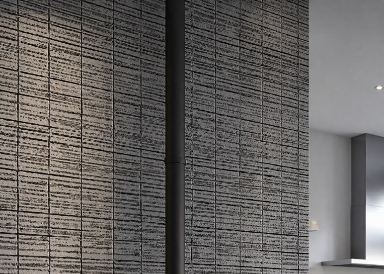 Nahaufnahme des dezentralen oberen Rauchabzugs vor einer Wand in markanter Stein- oder Fliesenstruktur.
