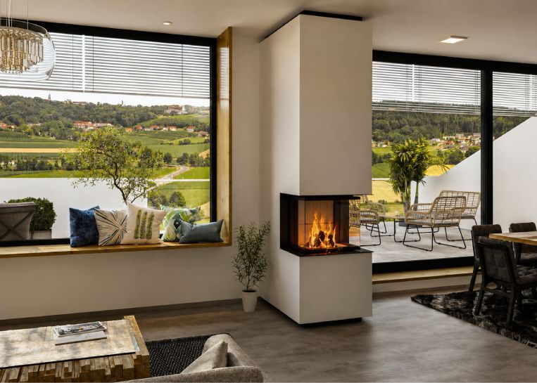 Eine moderne, raumhohe Kaminanlage Spartherm ARTE 3RLH 60 mit 3-seitiger Verglasung in einem hellen Wohnzimmer mit Panorama-Ausblick.