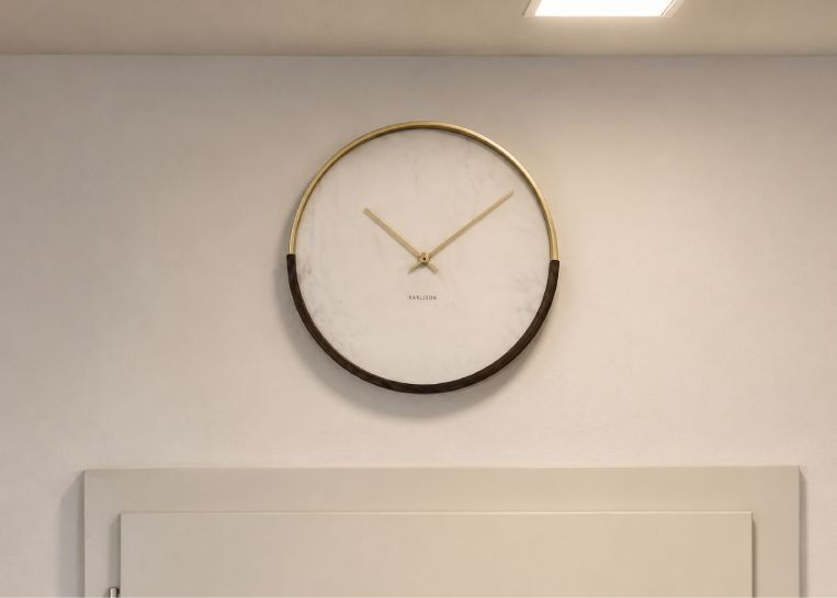 Detaillierte Ansicht einer minimalistischen Uhr aus Marmor und Holz an der weißen Wand über der Ofenanlage.