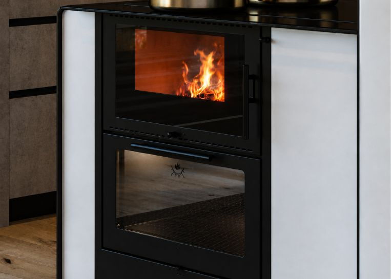 Nahaufnahme des lodernden Holzfeuers im Brennraum und des darunter liegenden Backrohrs mit Glasfront.