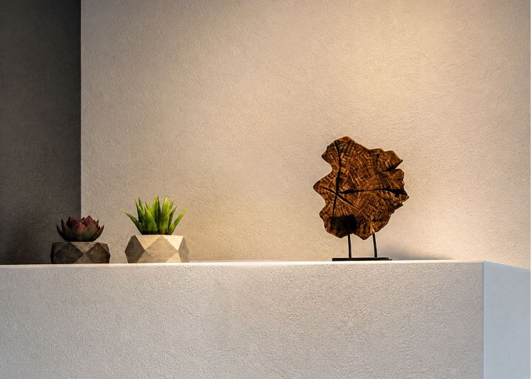 Detailansicht der mattweißen Keramikabdeckung mit einer abstrakten Holzskulptur und kleinen Sukkulenten als wohnliche Akzente.