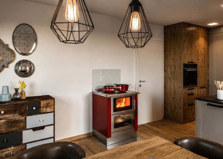 Ein moderner, weinroter Pertinger Tischherd BU70XL mit Edelstahl-Kochplatte und Sichtfenster, integriert in ein ländliches Küchendesign.