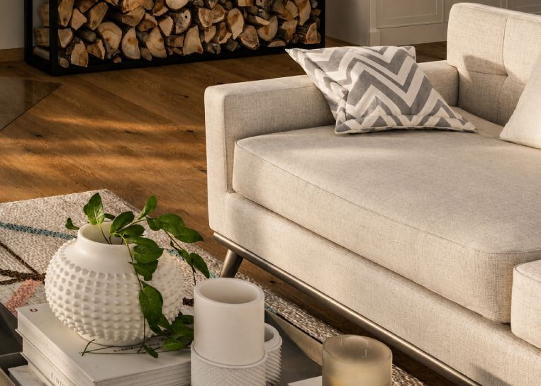 Ansicht aus der Wohnperspektive mit einem weißen Sofa im Vordergrund und dem dekorativen Holzlager im Hintergrund neben dem Kamin.