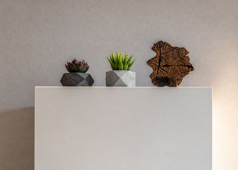 Detailansicht der pflegeleichten Feinsteinzeug-Abdeckung mit kleinen Sukkulenten in geometrischen Töpfen und einer Holzskulptur.
