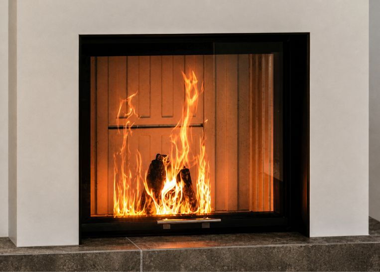 Nahaufnahme des lodernden Holzfeuers, das von einer massiven, schwarz lackierten Metallblende wie ein Bild eingerahmt wird.