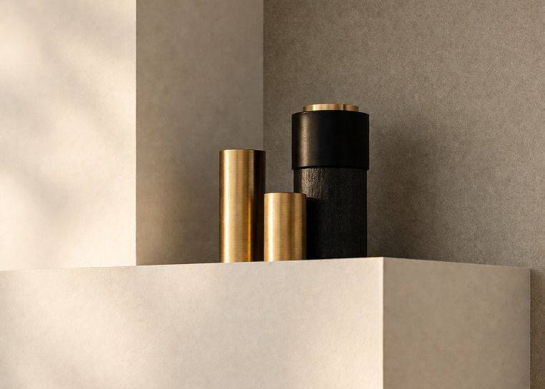 Nahaufnahme von modernen Vasen in Gold und Schwarz auf der pflegeleichten, mattweißen Keramikabdeckung der Kaminanlage.