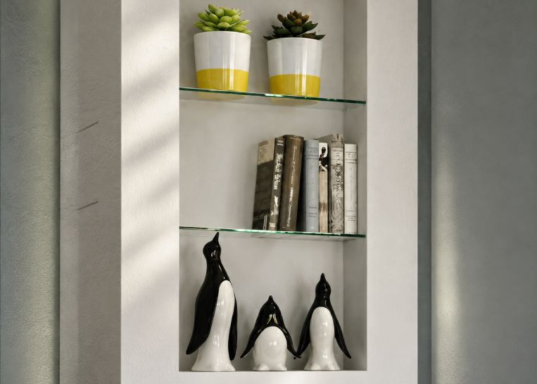 Nahaufnahme der in den Ofenbau integrierten Nische mit Glasfächern, Büchern und dekorativen Pinguin-Figuren.