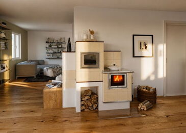 Ein hell gekachelter Aufsatzherd in der Küche mit Panorama-Sichtscheibe, Edelstahl-Reling und brennendem Holzfeuer.