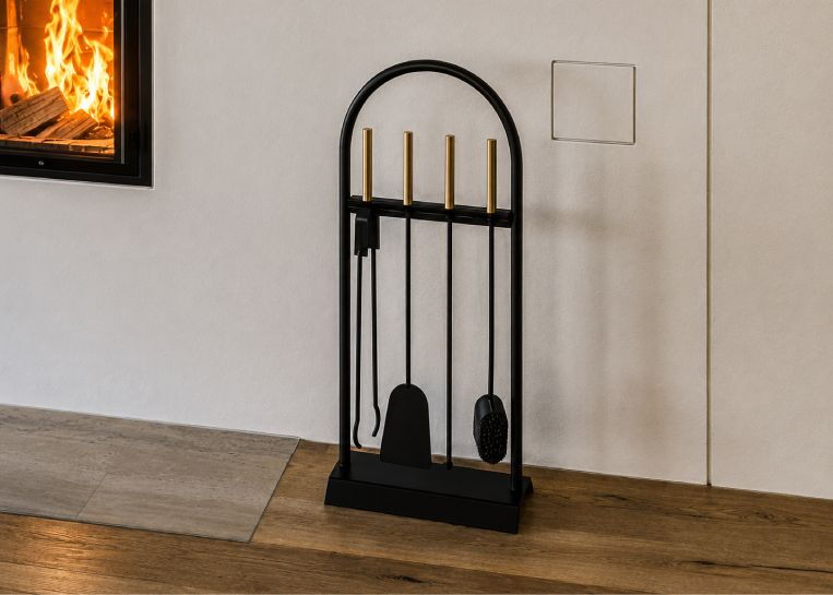 Stilvolles Kaminbesteck-Set in Schwarz mit goldenen Griffen, passend zum gradlinigen Design der Ofenanlage.