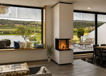 Eine moderne, raumhohe Kaminanlage Spartherm ARTE 3RLH 60 mit 3-seitiger Verglasung in einem hellen Wohnzimmer mit Panorama-Ausblick.