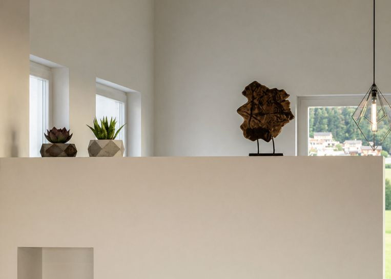 Detailansicht der pflegeleichten Kaminabdeckung mit modernen Sukkulenten in Betontöpfen und einer künstlerischen Holzskulptur.