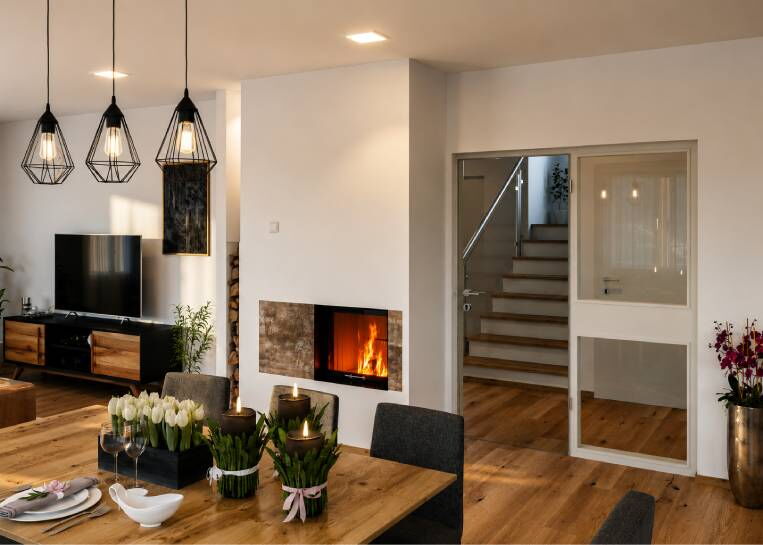 Perspektive auf den modernen Kamin als zentrales Element zwischen dem Esstisch und der Wohnlandschaft.