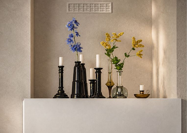 Nahaufnahme von schwarzen Vasen mit blauen und gelben Blumen sowie Kerzenständern auf der weißen, pflegeleichten Kaminabdeckung.