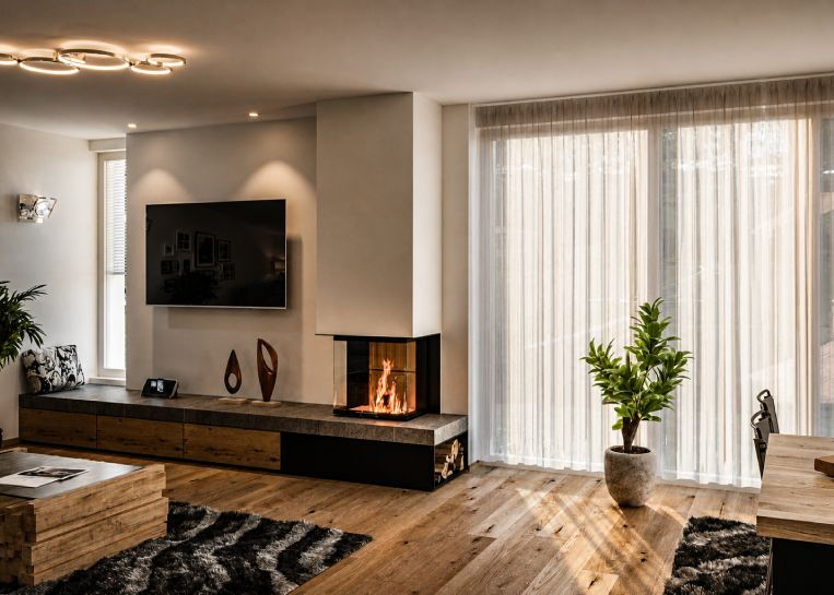Perspektive auf den deckenhohen Ofenkörper mit integrierter Metall-Holzbox und eleganten Keramik-Elementen im Wohnbereich.
