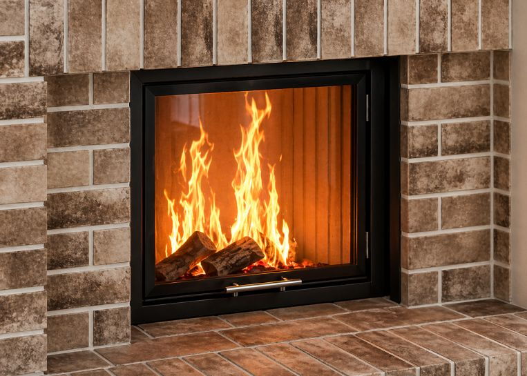 Detailansicht des brennenden Holzfeuers hinter der großen Sichtscheibe, umgeben von der strukturierten Oberfläche der gekalkten Klinker.